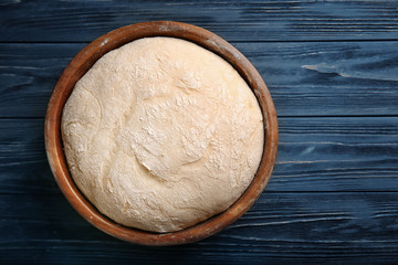 Bowl with fresh raw dough on wooden table