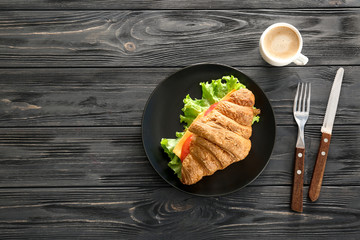 Plate with delicious croissant sandwich on table