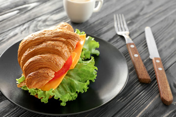 Plate with delicious croissant sandwich on table