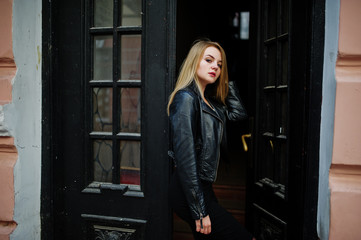 Fototapeta na wymiar Elegant blonde girl wear on black leather jacket posing at streets of town background old doors.