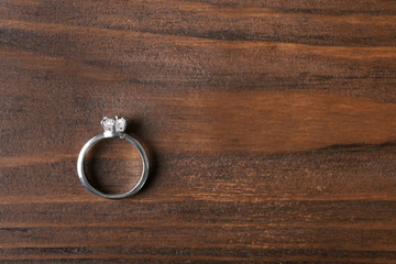 Luxury engagement ring with diamond on wooden background, top view