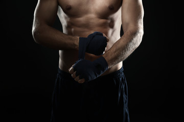 Fototapeta na wymiar Male boxer applying wrist wraps on black background, closeup