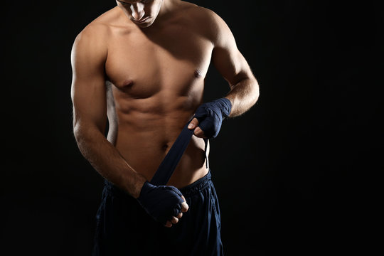 Male boxer applying wrist wraps on black background, closeup