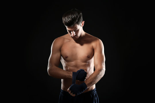 Male boxer applying wrist wraps on black background