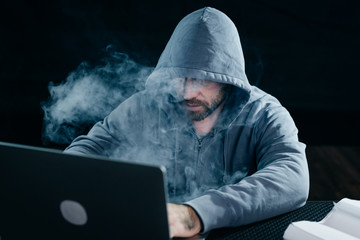 A computer hacker is typing on a smoking computer. Dark background