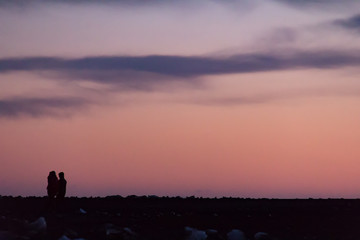Two people walking across a rocky landscape in silhouette against a colorfuly sky at sunset