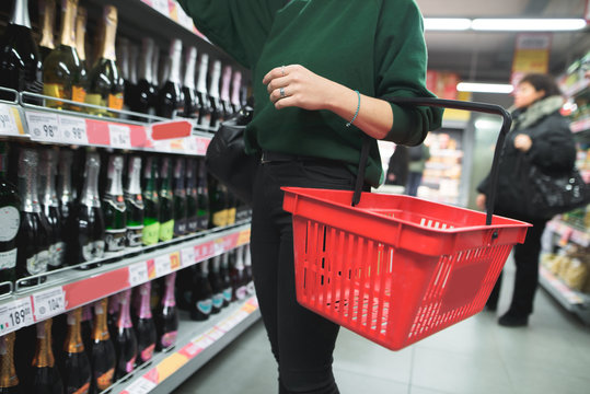 A woman with a red shopping bag chooses alcohol in a supermarket. Selection of products in the supermarket. The choice of wine in the store.