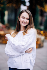 Happy white girl with long dark hair in sweater, garlands in bokeh, holiday cozy atmosphere, smiling woman with bengal lights, outdoor portrait
