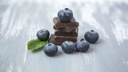 Fototapeta na wymiar Closeup Dark Chocolate Stack Fresh Organic Blueberries Fresh Mint Leaves on Wooden Background Natural Light Selective Focus 