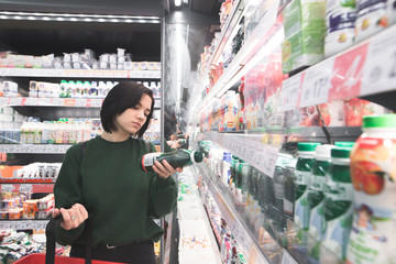 A beautiful girl reads a yogurt label in the supermarket milk department. The girl is shopping at the supermarket.