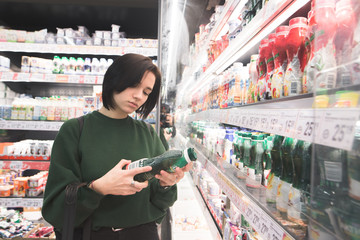 The girl buys dairy products in a supermarket. A young woman holds yogurt and reads the...