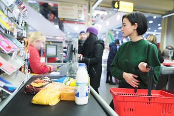 A beautiful girl stands at the supermarket and waits for a queue. The amount pays for purchases at the supermarket's cash desk.