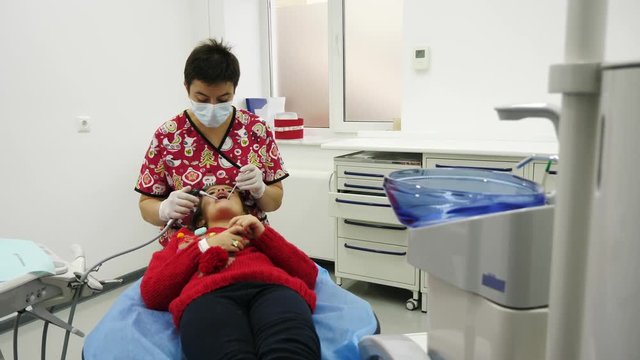 A little girl having her teeth cleaned at the dentist's. A dentist and little girl are dressed at clothes in the New Year's theme.