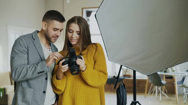 Professional photographer woman showing photos on digital camera to attractive model man in photo studio indoors