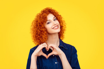 Love. Closeup portrait smiling happy young redhead curly hair woman making heart sign, symbol with...