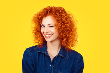 Winking. Closeup woman redhead curly hair smiling blinking eye to you camera isolated on yellow background. Happy life pictures, happiness - Powered by Adobe