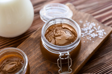 Jar with tasty caramel sauce on wooden board
