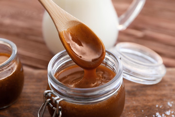Spoon with tasty caramel sauce and jar on board, closeup