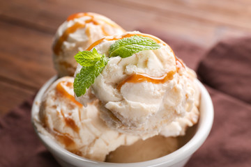 Delicious ice cream with caramel syrup in bowl on table