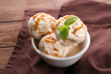 Delicious ice cream with caramel syrup in bowl on table