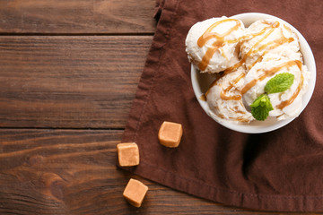 Delicious ice cream with caramel syrup in bowl on table