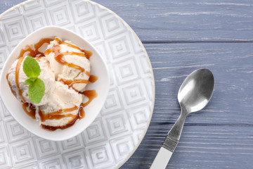 Delicious ice cream with caramel syrup in bowl on table
