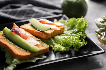Delicious sandwiches with cucumber and salmon fillet served with lettuce on plate, closeup