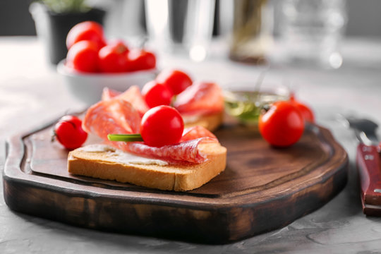 Delicious sandwich with cherry tomato and salami on wooden board, closeup