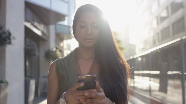 Attractive young woman walking in the city using her phone, in slow motion