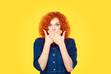 Censorship. Speak no evil concept. Concerned scared redhead woman curly afro hair covering her mouth with hands in blue jeans shirt isolated on yellow background