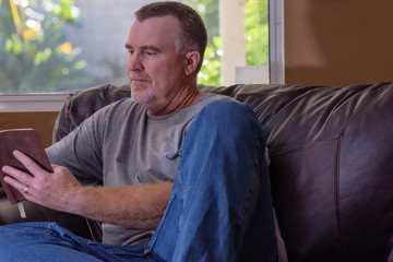 Mature male reads and relaxes in house on leather chair