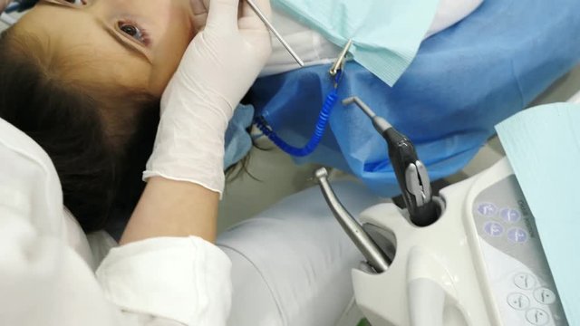 Dentist hands take from table a dental proba and examining a teeth of little girl. Dentist using a mirror and dental proba. Camera movement.