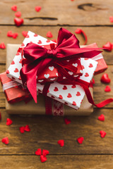 Stack of handcrafted gift boxes  with red bow ribbon and hearts on wooden table for Valentines day