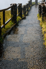 Wet aggregate concrete path of Victoria Falls with rock posts and wood fence rails
