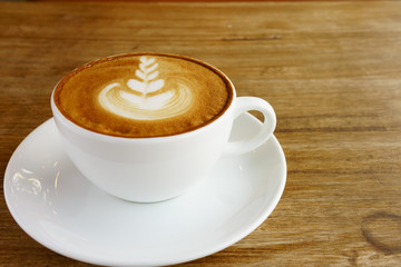 Coffee latte art in the white cup on the wooden floor.