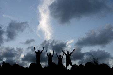 silhouette of happy kids raising their arm with sky background