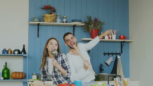 Slowmotion of Young joyful couple have fun dancing and singing while cooking in the kitchen at home
