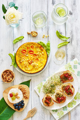 Vertical top view of healthy lunch or dinner on white talble. Omelet with young pea, bruchetta with sun dried tomato and pesto, cheese plate, walnut, lemonade and white wine.