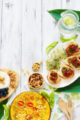 Vertical top view of healthy lunch or dinner on white table with copy space. Frittata with young peas, bruchetta with tomato and pesto, cheese plate and lemonade. 