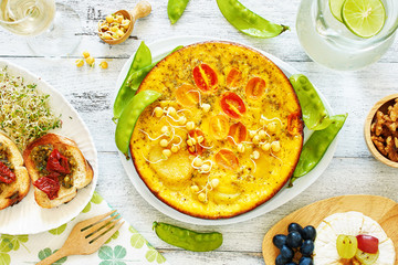 Frittata (omelet) with potato, tomato and pea sprouts, bruchetta, cheese plate and lemonade. Top view of brunch or lunch on a white table.