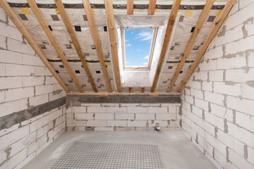 Mansard with environmentally friendly and energy efficient skylight window against blue sky. Room under construction with wooden beams, boards and windows
