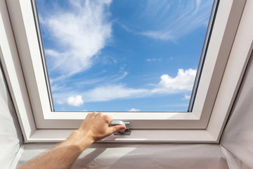 Man close new skylight (mansard window) in an attic room against blue sky - Powered by Adobe