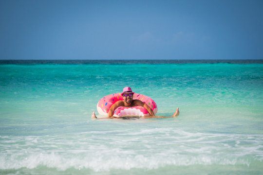 Happy handsome funny man in pink hat is swimming on inflatable tube on the coast of Caribbean Sea in summer sunny day