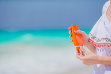 Suncream bottle in female hands on the beach.