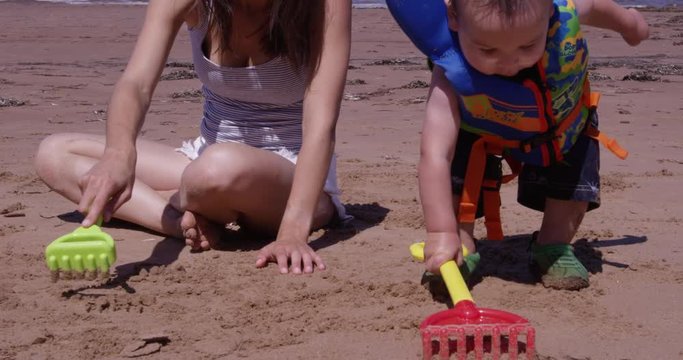 Mother and Toddler raking beach sand - close up