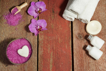 Spa background with orchid, rose bath salt, body lotions and white towels on a wooden table with copy space for your text