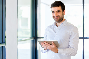Young handsome businessman using his touchpad standing in office