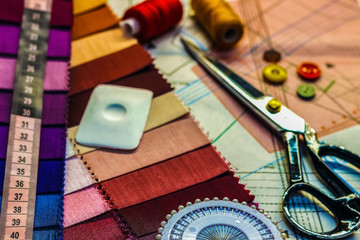 Workplace tailor. On the table close-up lie the samples of fabrics, scissors, thread, balac, roulette and buttons.