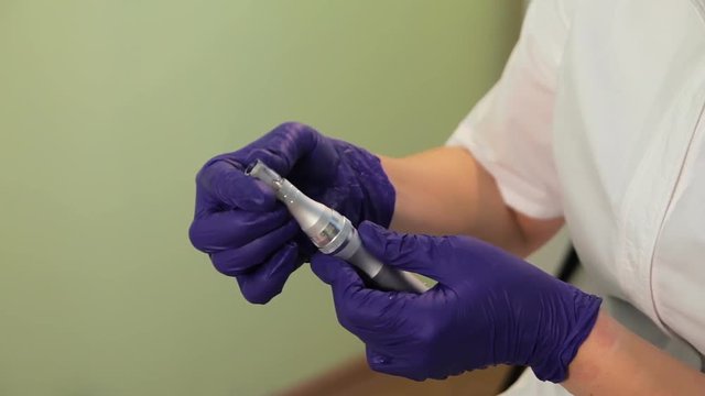 The beautician sets disposable applicator for mesotherapy in the device. The hands of the beautician gloves in closeup. Derma pen