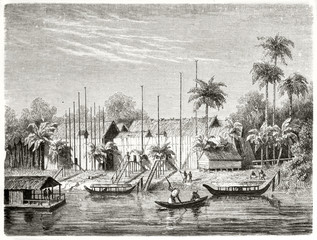 Ancient river in the jungle flowing near to a native Dayak people village, Borneo. Boats sailing and palms on background. Created by Francais after Schwaner published on Le Tour du Monde Paris 1862 - 185332753